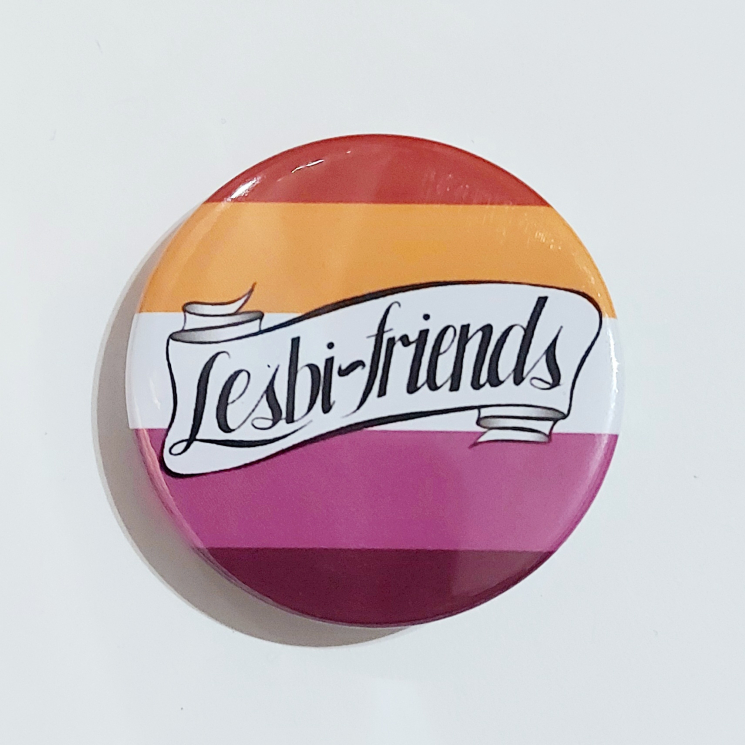A round badge featuring a banner that reads "Lesbi-friends" over lesbian flag