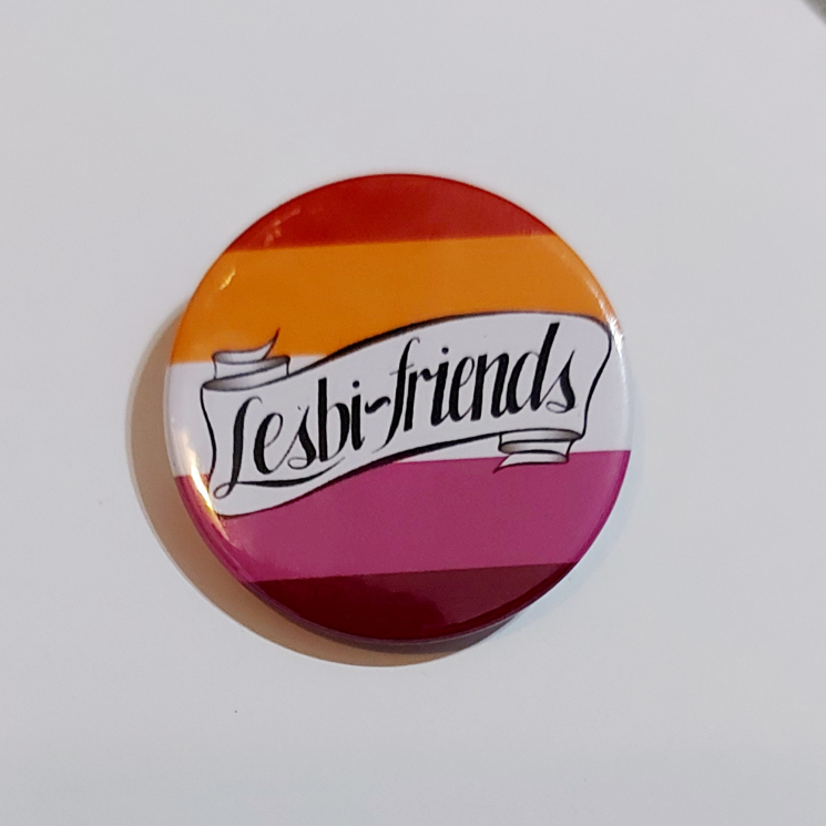 A round badge featuring a banner that reads "Lesbi-friends" over lesbian flag