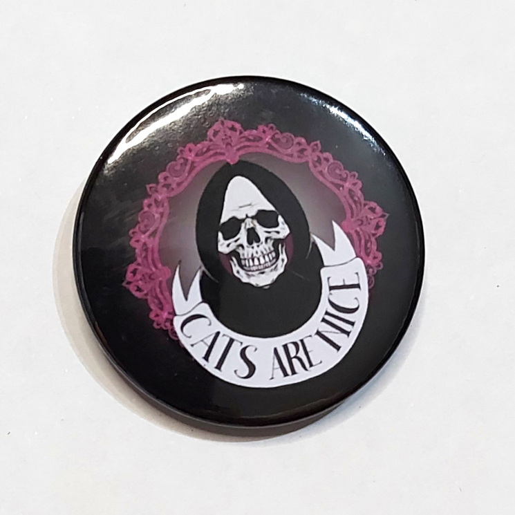 Badge with a grinning skull in a hood and a banner that reads "Cats Are Nice"