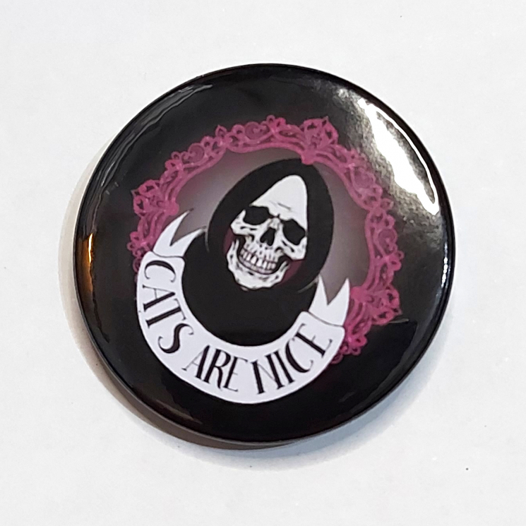 Badge with a grinning skull in a hood and a banner that reads "Cats Are Nice"