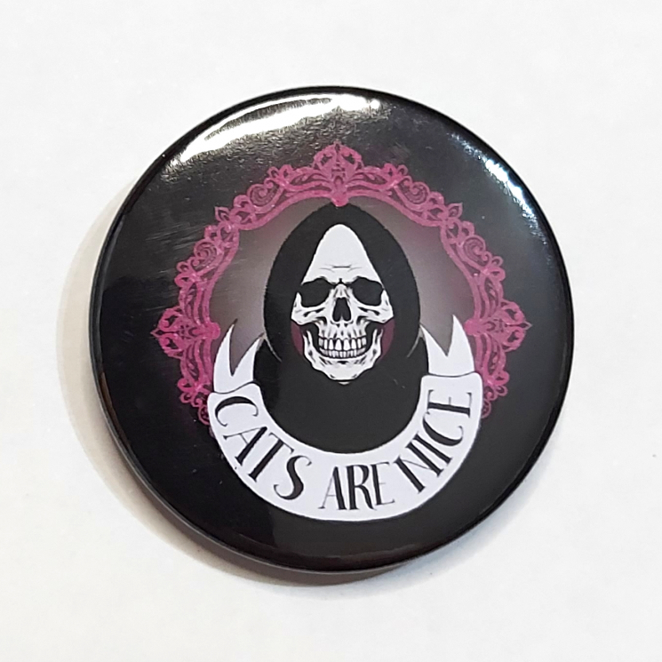Badge with a grinning skull in a hood and a banner that reads "Cats Are Nice"